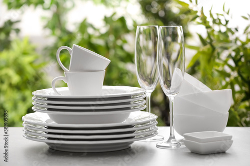 Set of clean dishware and champagne glasses on grey table against blurred background