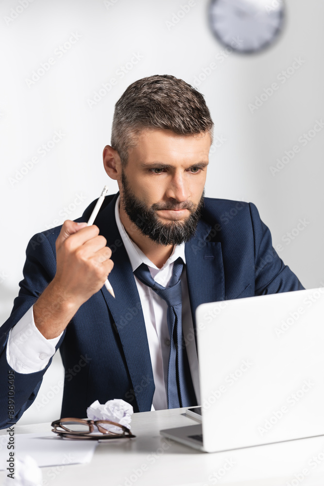 Stressed businessman holding broken pencil near gadgets, clumped paper and eyeglasses on blurred foreground in office Stressed businessman holding broken pencil near gadgets, clumped paper and eyeglasses on blurred foreground in office