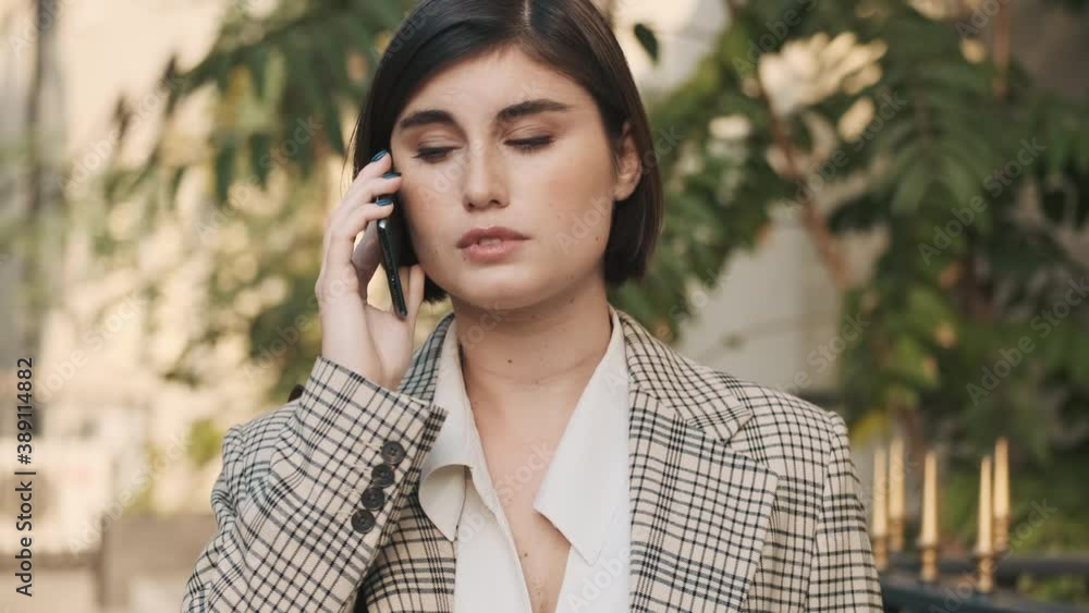 Tracking shot of stylish businesswoman looking confident talking on phone on city street Tracking shot of stylish businesswoman looking confident talking on phone on city street