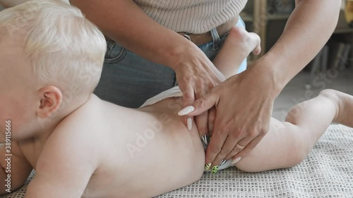 Close up of unrecognizable woman standing at changing table and changing nappy on blond-haired Caucasian baby boy lying on it