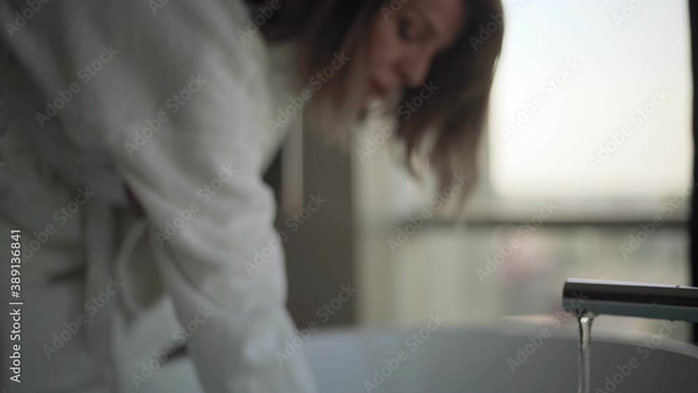 Woman touching water from modern bathtub faucet Woman touching water from modern bathtub faucet