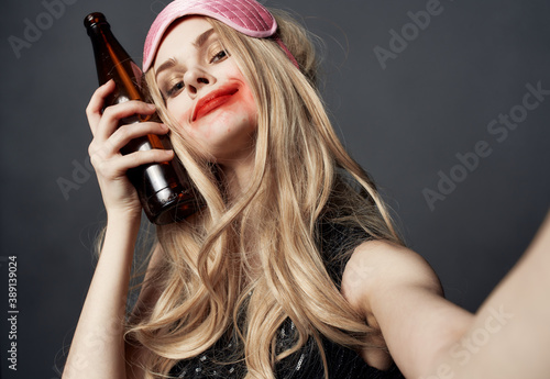 Drunk woman with a bottle of beer on a gray background gestures with her hands and bright makeup