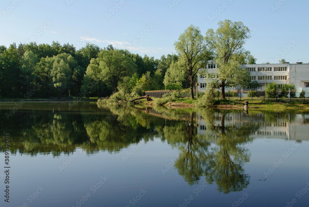 Ramenskoe. Moscow region. Russia. June 12. 2017. The school building is reflected in the water of a small pond on a Sunny morning.