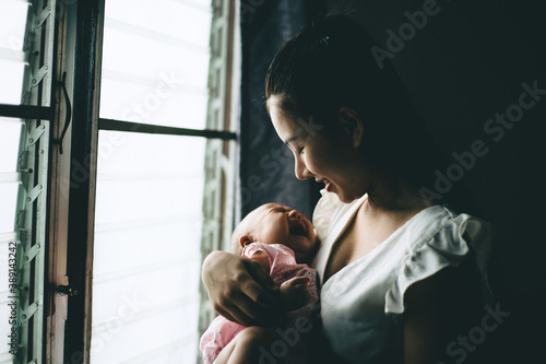 An Asian mother held and watched the baby smiling happily at the window low key dark tone.