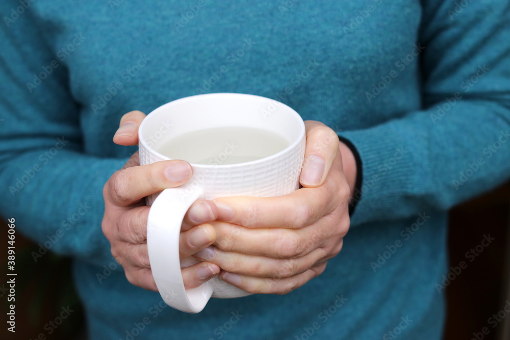 Woman holding a mug of hot water, warming her cold hands Woman holding a mug of hot water, warming her cold hands