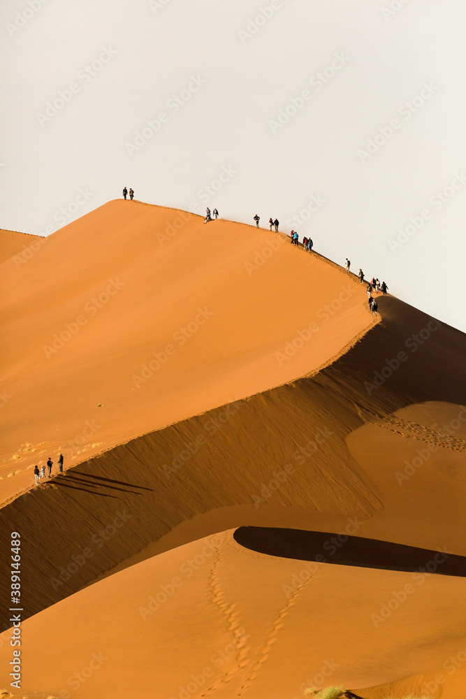 Tourists climbing a large red sand dune in Sossusvlei, Namibia. Stock ...