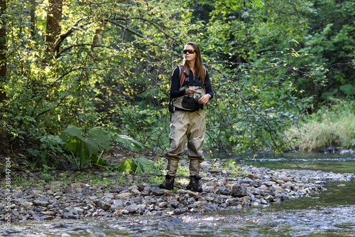 Woman fishes on the river catching fish, pulling rod while fishing at the weekend. Fisherman with rod, spinning reel on the river bank. Fishing for salmo.