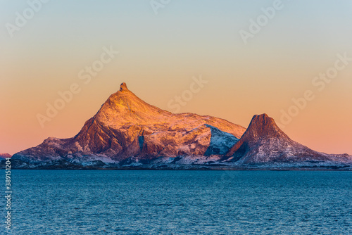 Snow covered mountain in amazing colorful sunrise light over Norwegian sea seen from small cruise ship on clear winter day