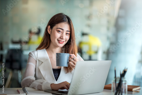 Young asian businesswoman on a coffee break and using laptop computer in office.