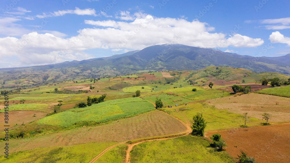 Fertile farmlands with growing crops and mountains with clouds against a blue sky. Mindanao, Philippines.