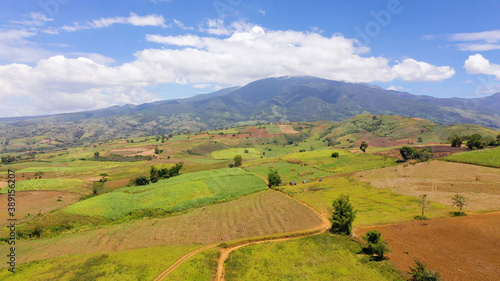 Fertile farmlands with growing crops and mountains with clouds against a blue sky. Mindanao, Philippines.