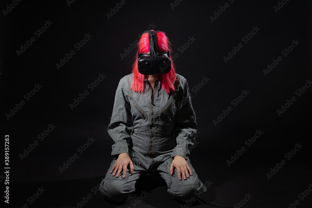 young woman with pink hair and in a jumpsuit uses virtual reality glasses, is in the game,