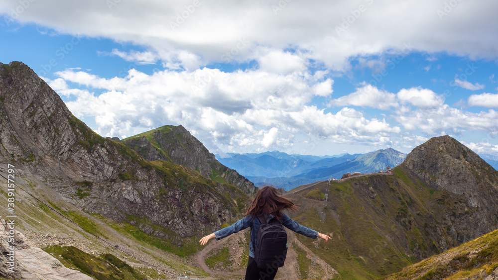 A young female tourist on top of a mountain on the panorama background.