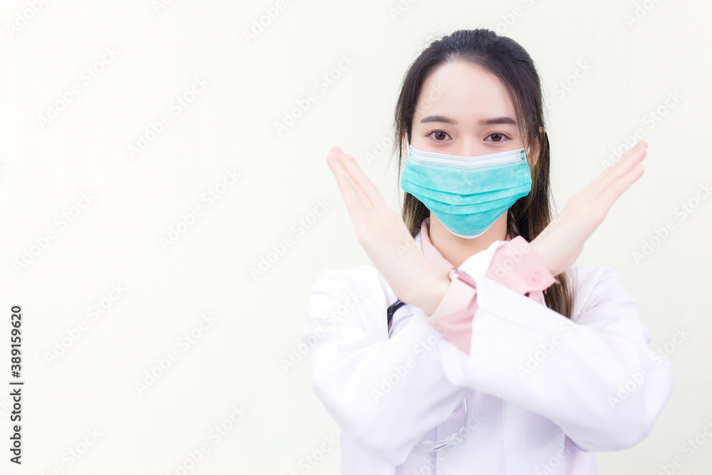 Asian woman doctor wears medical face mask while shows hand in stop sign (stop mark) on blank background.