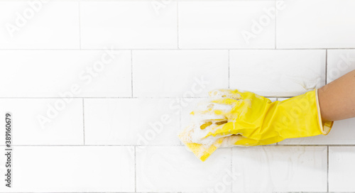 A female hand in a yellow latex glove sponges a tile. There is a lot of foam in the sink. The concept of cleaning the bathroom or kitchen, cleanliness. Copyspace.