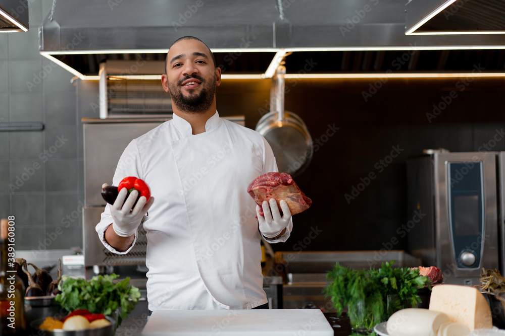 Happy smiling chef prepares meat dish with various vegetables in the Happy smiling chef prepares meat dish with various vegetables in the
