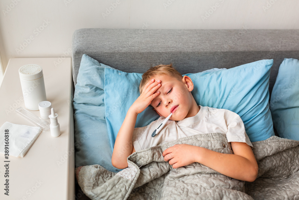 Sick little boy with high fever and headache laying in bed and holding thermometer in his mouth. Stay at home during corona virus epidemic Sick little boy with high fever and headache laying in bed and holding thermometer in his mouth. Stay at home during corona virus epidemic