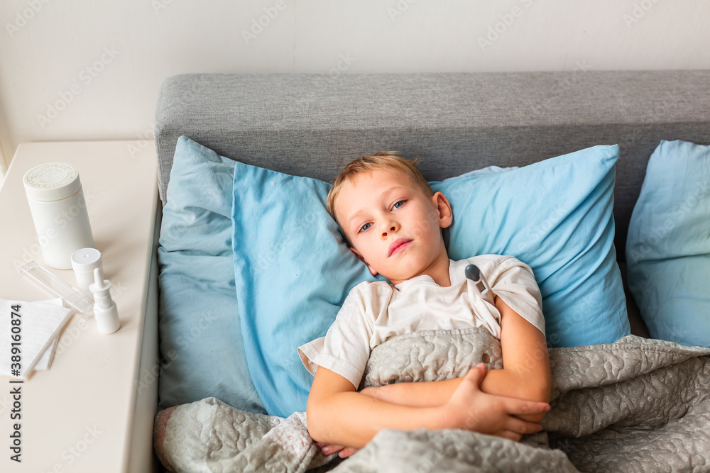 Sick little boy with high fever and headache laying in bed and holding thermometer. Stay at home during corona virus epidemic Sick little boy with high fever and headache laying in bed and holding thermometer. Stay at home during corona virus epidemic