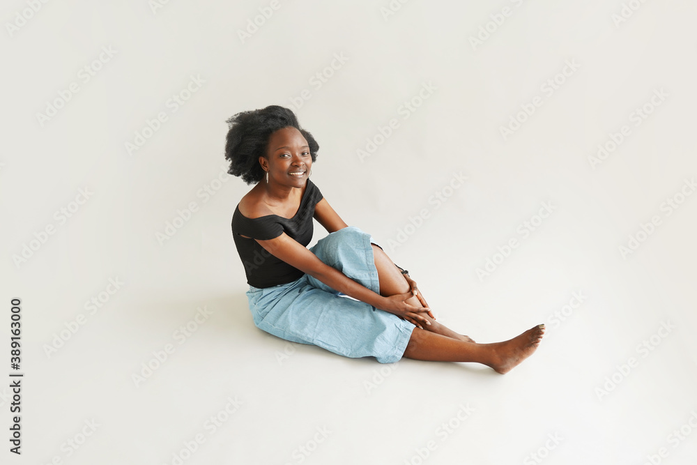 Cheerful Young African American Woman Sitting on the Floor on White Background In Studio Cheerful Young African American Woman Sitting on the Floor on White Background In Studio