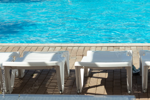 White sun loungers by the pool with blue bright water  copy space
