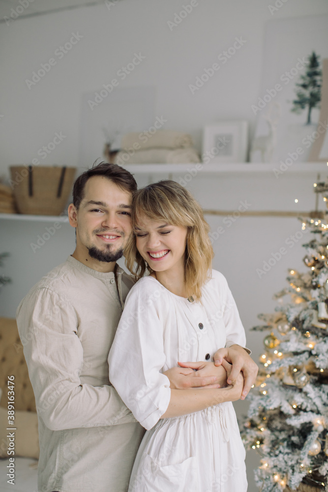 Happy young couple hugging near decorated Christmas tree at light modern interior. Happy young couple hugging near decorated Christmas tree at light modern interior.