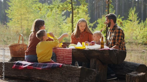 Families with children on a picnic in a resting place in a sunny forest, enjoying a vacation in nature