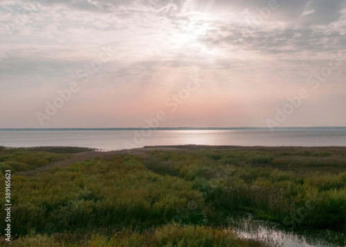 view of the lake before sunset  sunbeams through the clouds  calm water surface  lake meadow foreground