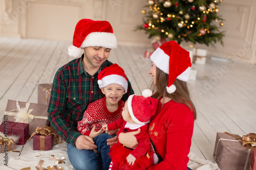 Christmas family Happy mom,dad and little daughter and son on Santa Claus hat. Enjoying love hugs, holidays people. Christmas tree with garlands in decorated room background. Togetherness concept