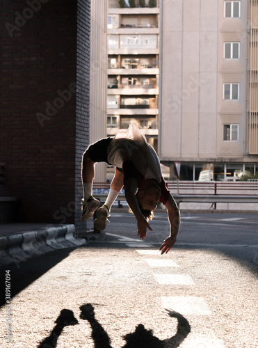 young boy caucasian short curly hair doing flips dancing doing break dance backflip flic flac dark bridge street city photo