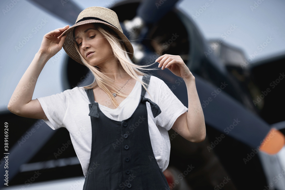 woman in a straw hat on the background posing against the backdrop of an airplane with a propeller