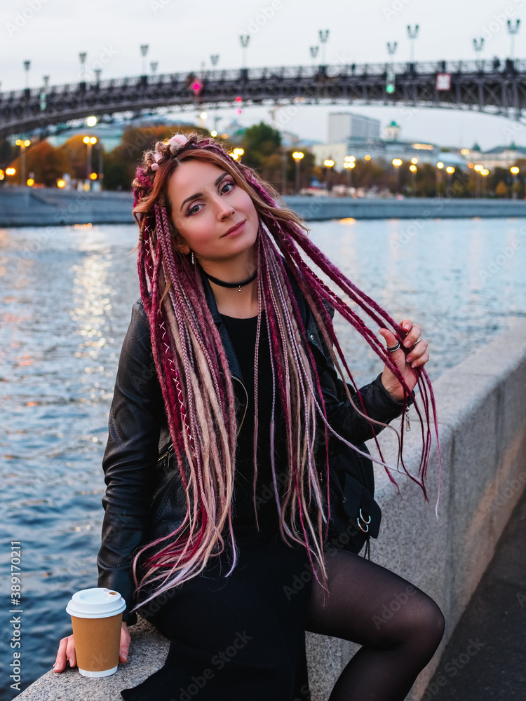 beautiful young woman with long pink and beige dreadlocks in black clothes on the bank of the Moskva River