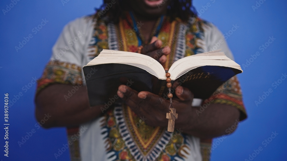 Unrecognizable African black man in traditional dress with rosary reading the Holy Bible . High quality photo