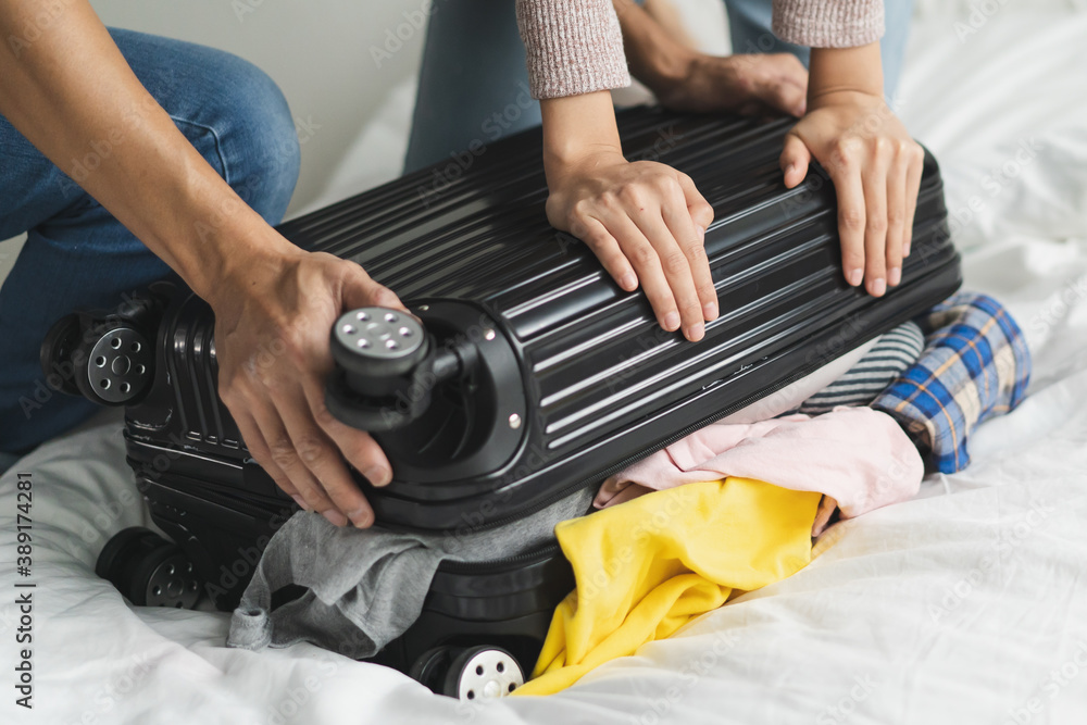 couple trying to close overload suitcase because too many things in the