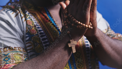 Unrecognizable African black man in traditional dress with rosary praying with hands over his chests. High quality photo
