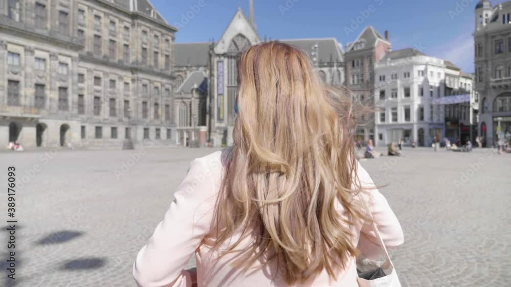 Beautiful woman walks across sunny Dam Square in Amsterdam with mask, wide tracking