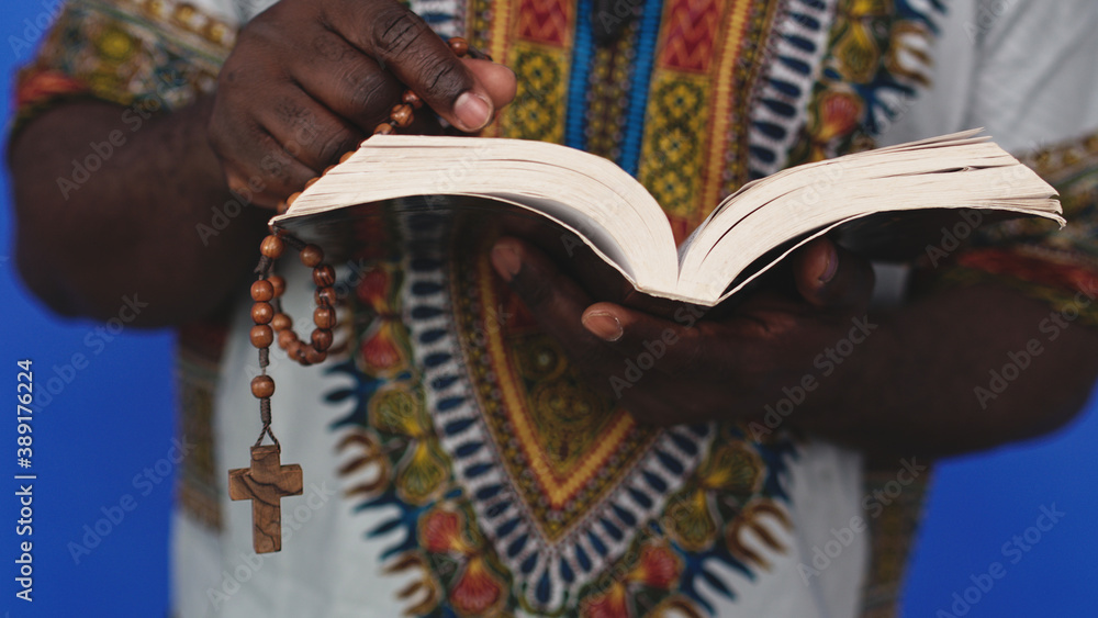 Unrecognizable African black man in traditional dress with rosary reading the Holy Bible . High quality photo