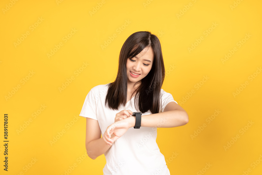 Asian young woman wearing white t-shirt standing and looking at her smartwatch Asian young woman wearing white t-shirt standing and looking at her smartwatch