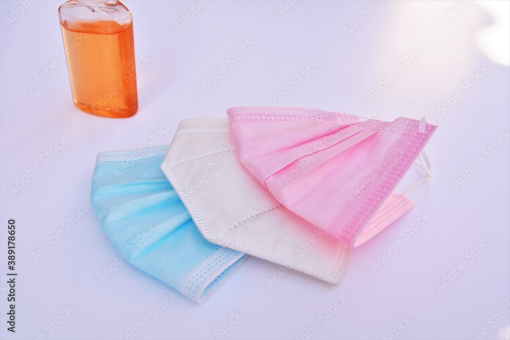 Pink, blue and white surgical masks with orange hydroalcoholic gel in a white background for coronavirus pandemic Pink, blue and white surgical masks with orange hydroalcoholic gel in a white background for coronavirus pandemic