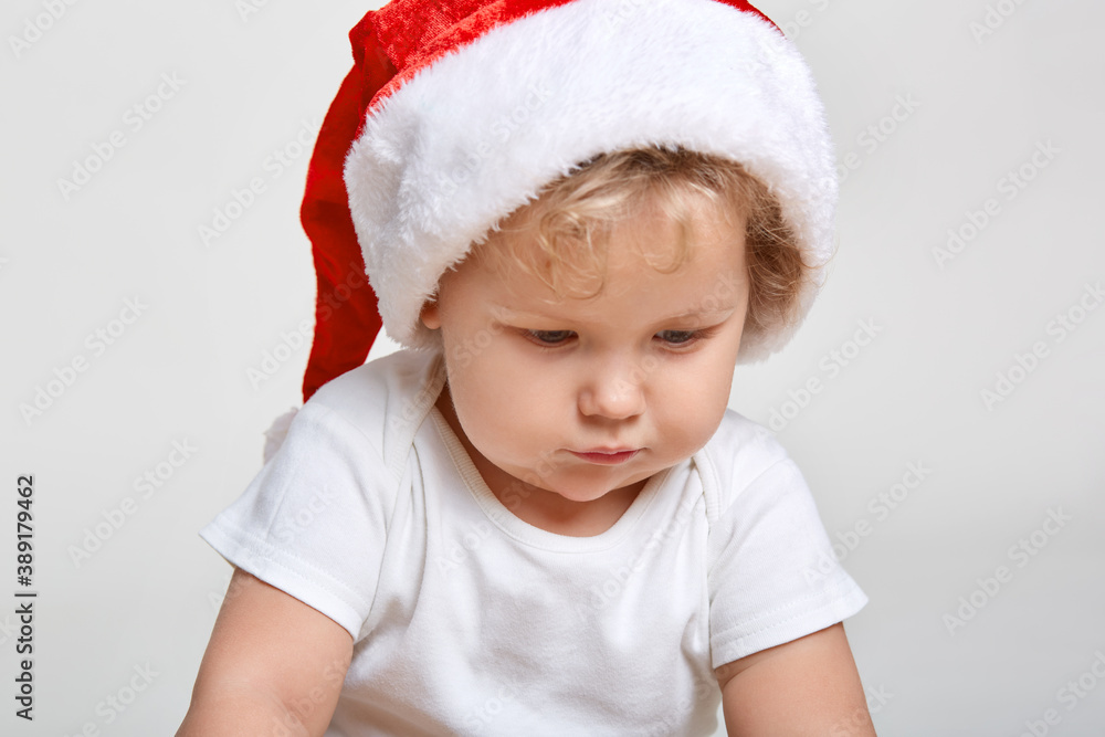 Little baby in red cap of Santa Claus celebrates Christmas, infant in red cap, New Year's holidays, cute kid looking away, posing isolated over white background. Little baby in red cap of Santa Claus celebrates Christmas, infant in red cap, New Year's holidays, cute kid looking away, posing isolated over white background.