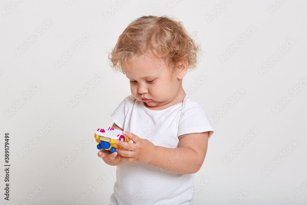 Blond toddlers playing with color car isolated on white background, looking concentrated at toy in his hands, wearing t shirt, male child with curly hair. Blond toddlers playing with color car isolated on white background, looking concentrated at toy in his hands, wearing t shirt, male child with curly hair.