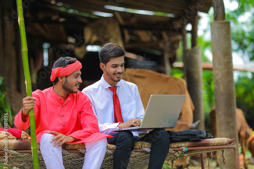 Young indian agronomist showing some information to farmer in laptop at home