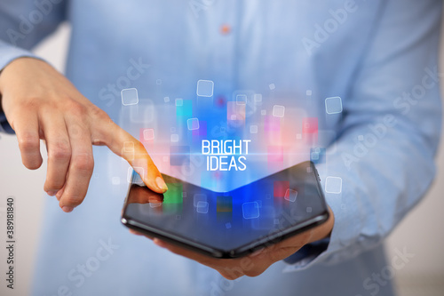 Young man holding a foldable smartphone with BRIGHT IDEAS inscription, educational concept