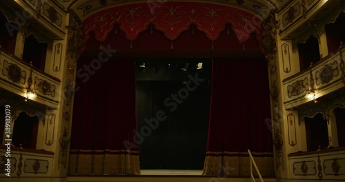Cinematic shot of empty classic theatre with red velvet curtains opening stage with dramatic lighting before start of show.