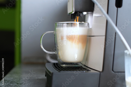 A coffee machine pours espresso into a glass cup with milk.