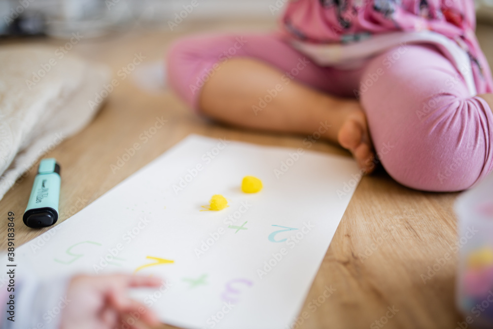 Little girl legs sitting on the wooden floor and doing sums on a paper sheet Little girl legs sitting on the wooden floor and doing sums on a paper sheet