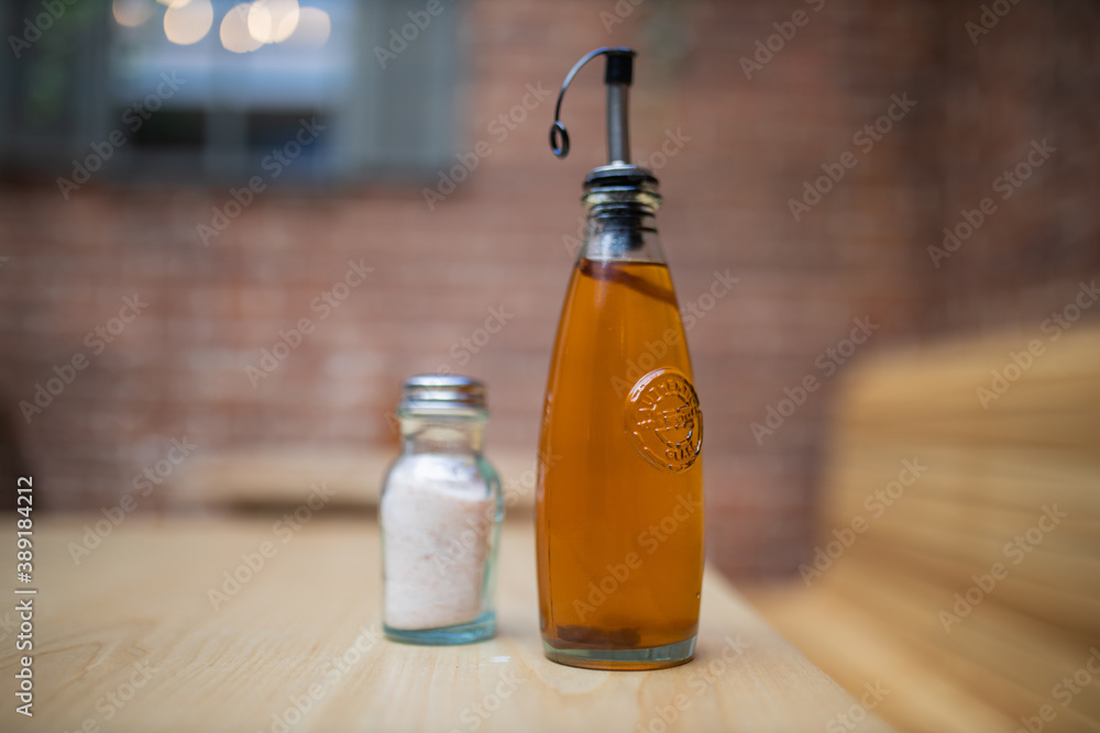 A bottle of salad dressing and a salt jar on a wooden restaurant table A bottle of salad dressing and a salt jar on a wooden restaurant table
