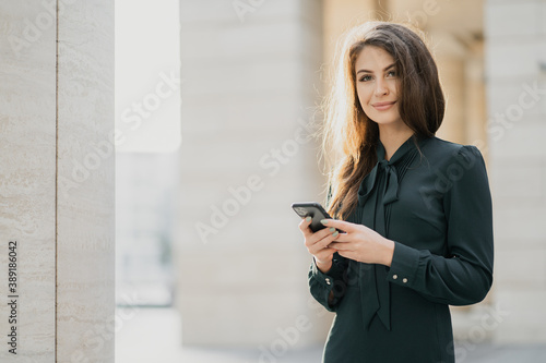 posing for a portrait of a young female student of Caucasian appearance, a brunette in a stylish green dress. smiling and looking at the camera, typing to a friend on a new phone.