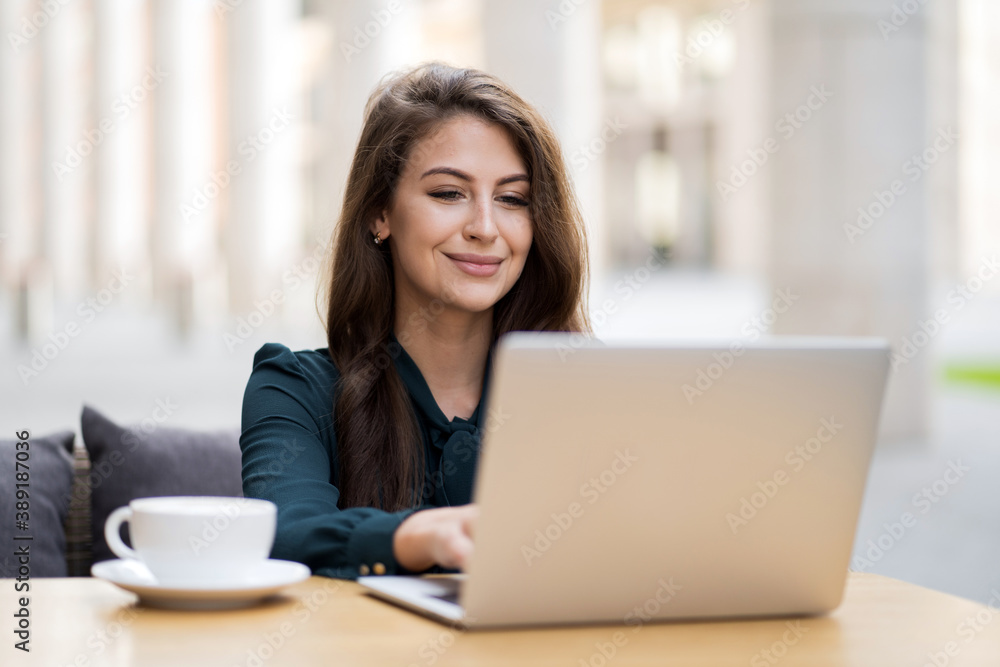 a young teacher does lessons remotely online on a laptop. Sitting in a summer cafe alone with a white Cup of tea coffee Americano latte a young teacher does lessons remotely online on a laptop. Sitting in a summer cafe alone with a white Cup of tea coffee Americano latte