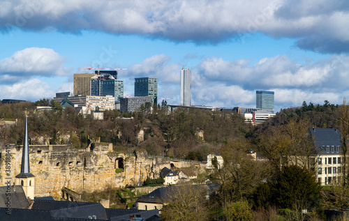 View of the city of Luxembourg, Europe with a church tower, houses, forests, the fortress wall (Corniche) and the Kirchberg business district in the background.jpg