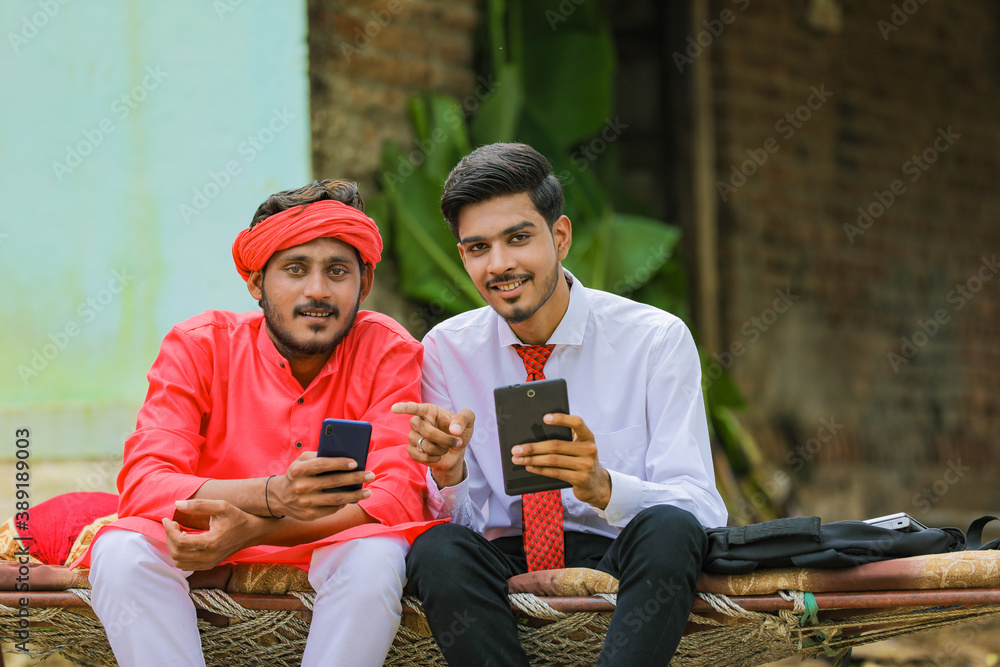 Obraz premium Young indian agronomist or banker showing some information to farmer in smartphone
